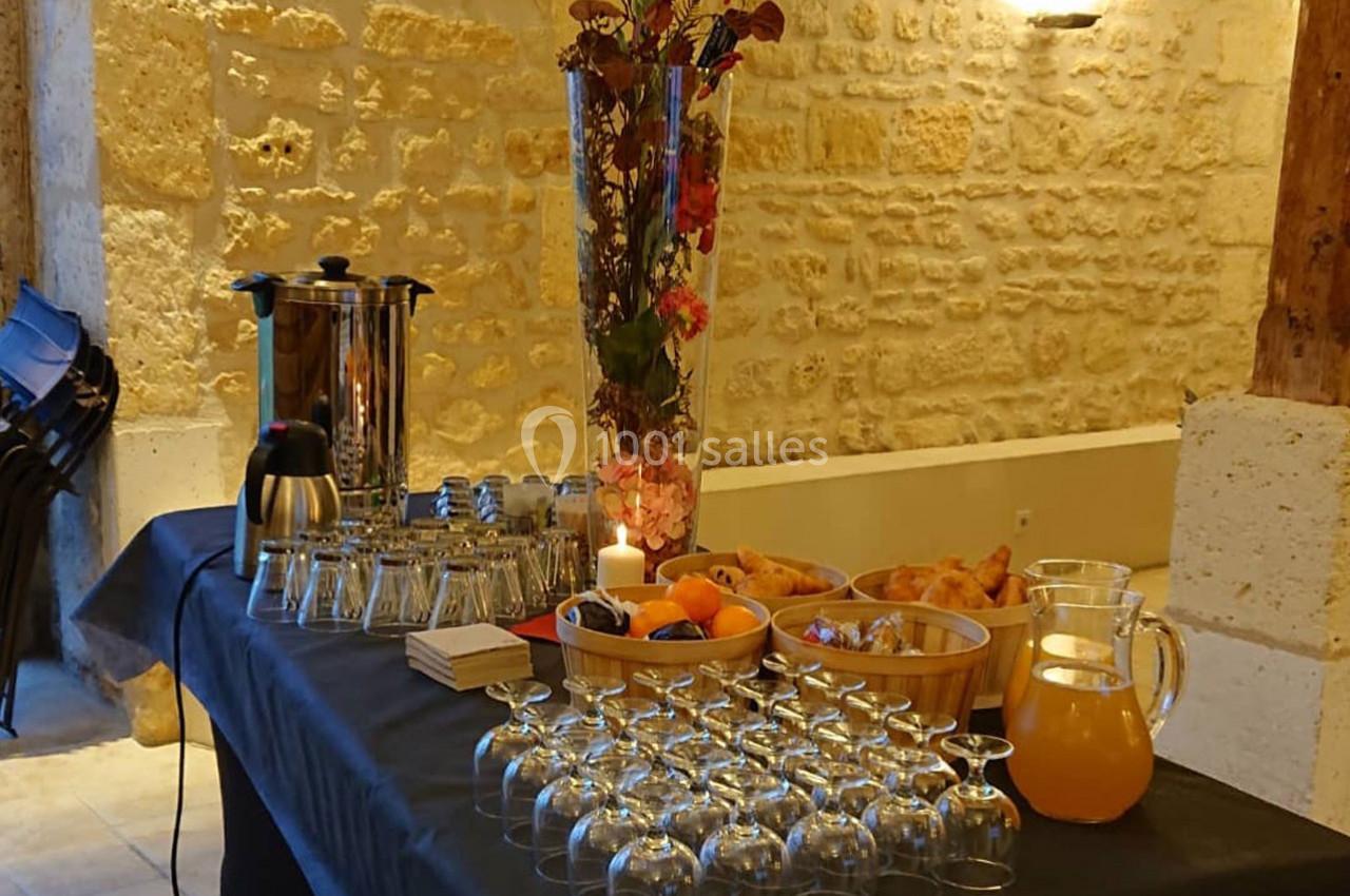 Table dressée avec des verres, une carafe de jus, une cafetière, des viennoiseries et une décoration florale.