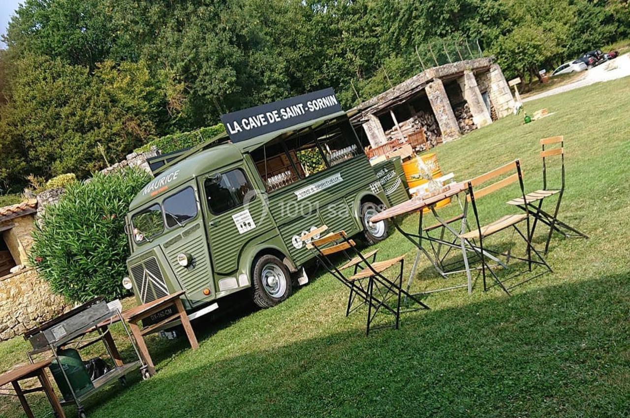 Camion rétro vert aménagé en food truck, stationné sur une pelouse avec des tables et chaises pliantes autour.