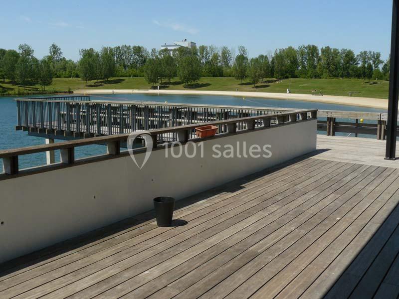 Terrasse en bois avec vue sur un lac, des pontons et une pelouse arborée en arrière-plan.