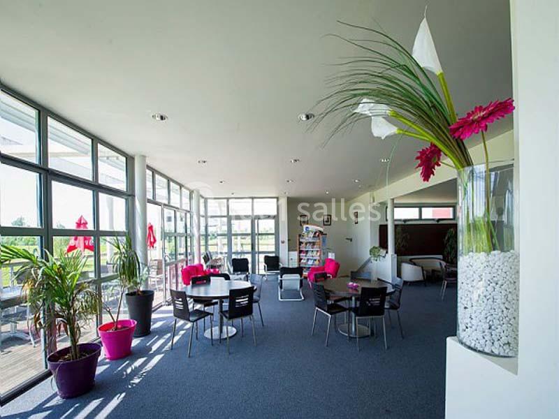 Salle lumineuse avec grandes baies vitrées, mobilier moderne, plantes décoratives et vue sur une terrasse extérieure.