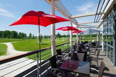 Terrasse en bois avec mobilier de jardin, parasol et vue sur un terrain de golf verdoyant par temps ensoleillé.