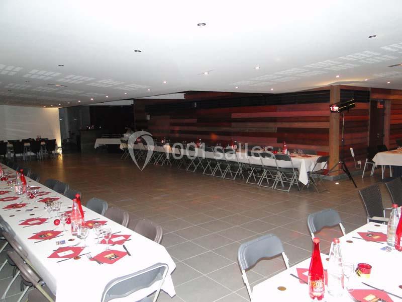 Salle de réception avec tables dressées, chaises pliantes et éclairage tamisé.