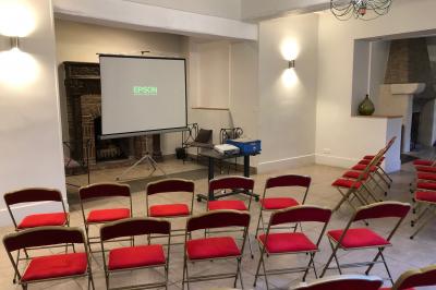 Salle lumineuse avec une grande table rectangulaire couverte d'une nappe bleue, entourée de chaises rouges, et une fenêtre…