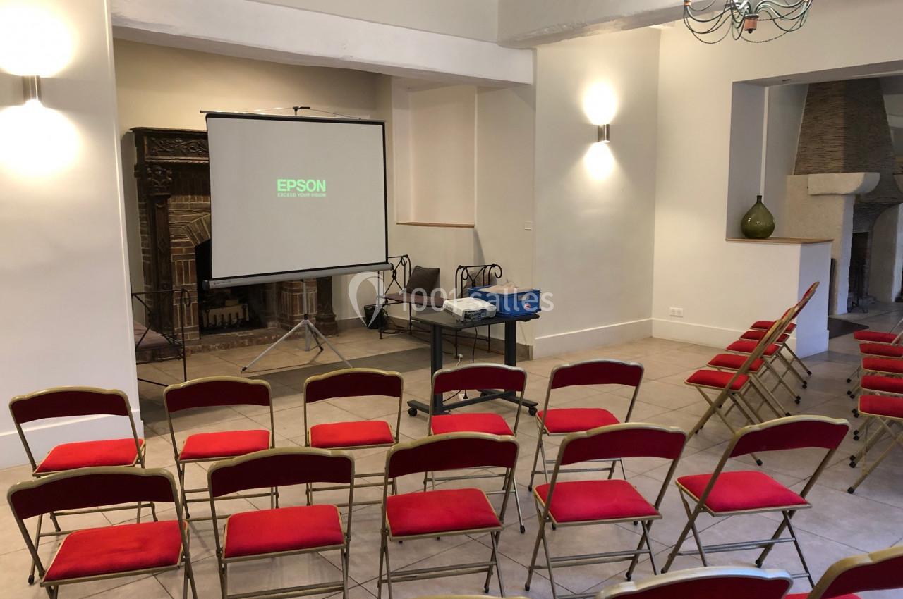 Salle de réunion avec des chaises rouges alignées, un projecteur Epson et un écran de projection.