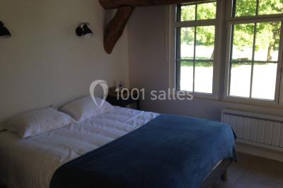 Salle lumineuse avec une grande table rectangulaire couverte d'une nappe bleue, entourée de chaises rouges, et une fenêtre…
