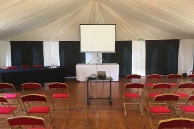 Salle lumineuse avec une grande table rectangulaire couverte d'une nappe bleue, entourée de chaises rouges, et une fenêtre…