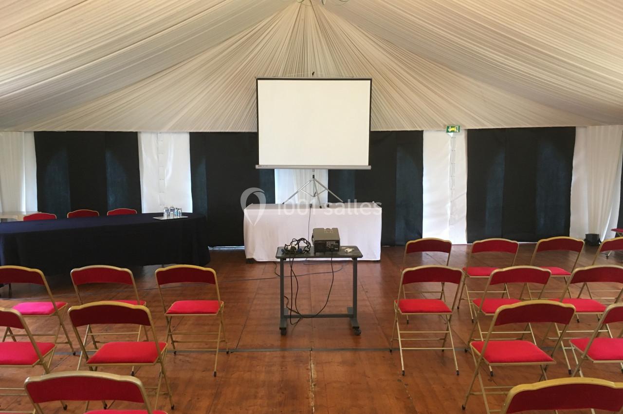 Salle de conférence avec chaises rouges alignées, écran de projection et matériel audiovisuel sur un chariot.