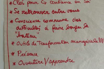 Salle lumineuse avec une grande table rectangulaire couverte d'une nappe bleue, entourée de chaises rouges, et une fenêtre…