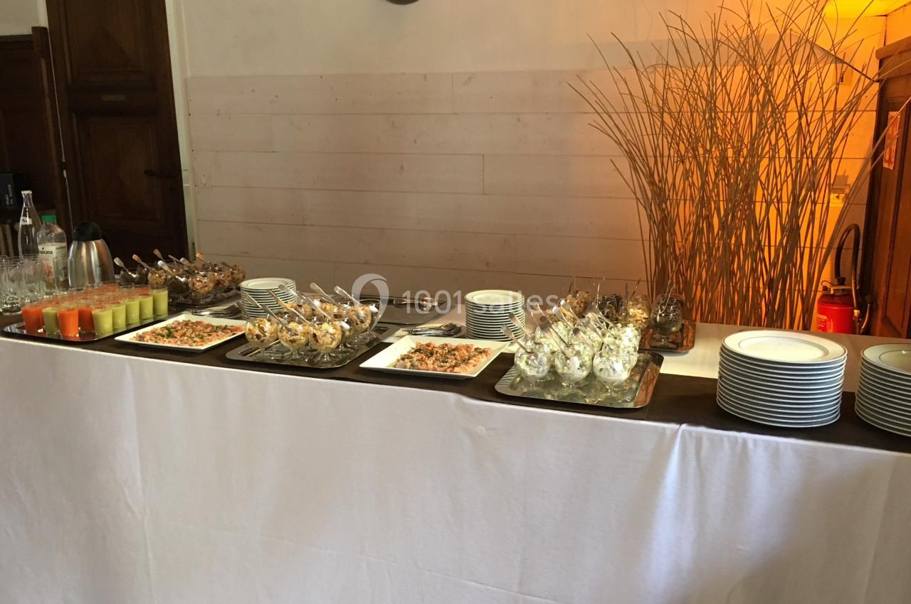 Buffet avec verrines, plats variés, assiettes empilées et décoration de branches dans un cadre intérieur.