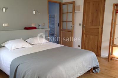 Salle lumineuse avec une grande table rectangulaire couverte d'une nappe bleue, entourée de chaises rouges, et une fenêtre…