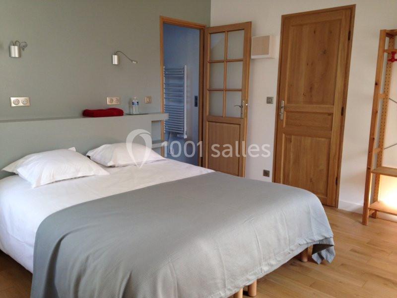 Chambre avec lit double, couvre-lit gris, murs clairs, éclairage mural et portes en bois.