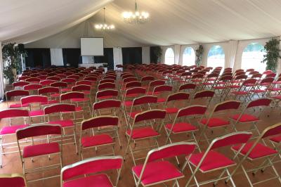 Salle lumineuse avec une grande table rectangulaire couverte d'une nappe bleue, entourée de chaises rouges, et une fenêtre…