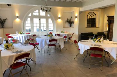 Salle lumineuse avec une grande table rectangulaire couverte d'une nappe bleue, entourée de chaises rouges, et une fenêtre…