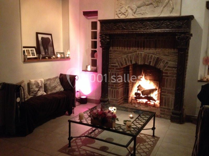 Salon chaleureux avec cheminée en pierre allumée, canapé brun, table basse en verre et décorations cosy.