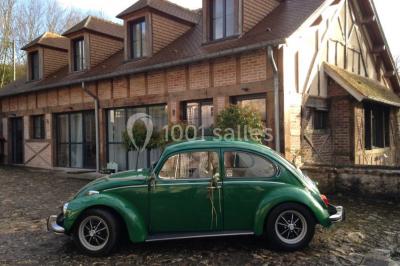 Salle lumineuse avec une grande table rectangulaire couverte d'une nappe bleue, entourée de chaises rouges, et une fenêtre…