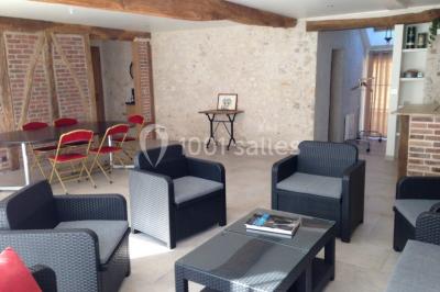 Salle lumineuse avec une grande table rectangulaire couverte d'une nappe bleue, entourée de chaises rouges, et une fenêtre…