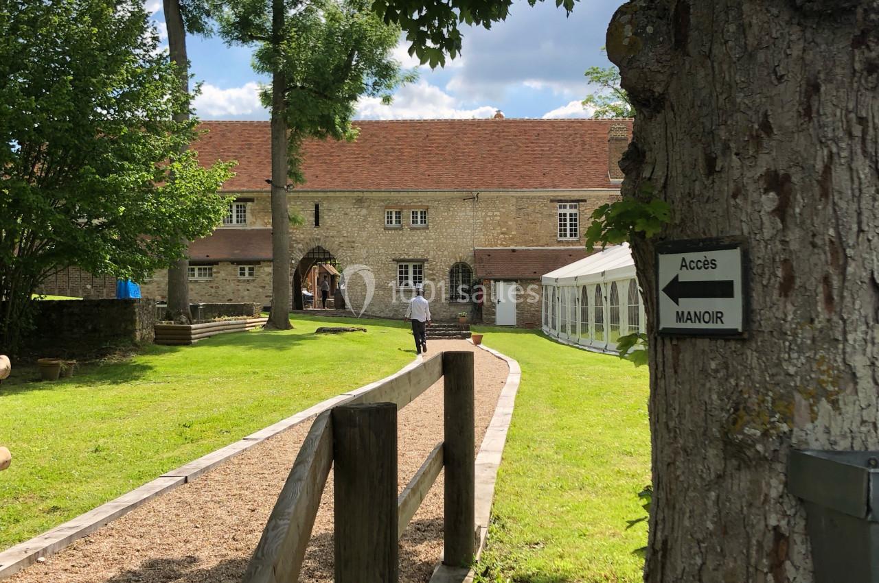 Chemin en gravier menant à un manoir en pierre, avec un panneau indiquant l'accès, entouré de verdure.