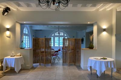 Salle lumineuse avec une grande table rectangulaire couverte d'une nappe bleue, entourée de chaises rouges, et une fenêtre…