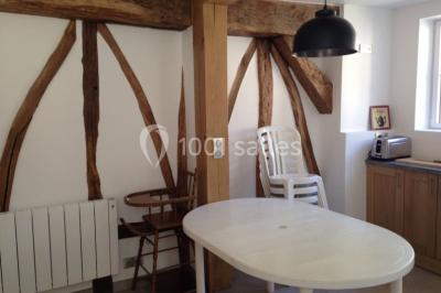Salle lumineuse avec une grande table rectangulaire couverte d'une nappe bleue, entourée de chaises rouges, et une fenêtre…