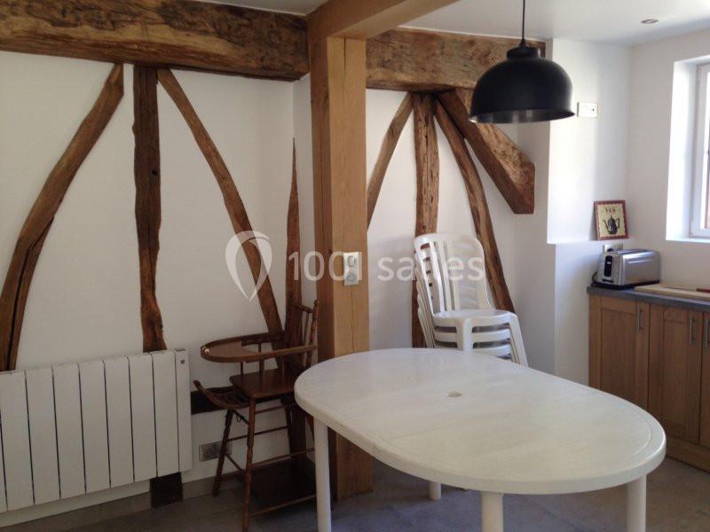 Cuisine avec poutres apparentes en bois, table blanche, chaise en bois, chaises empilées et électroménager sur un plan de…