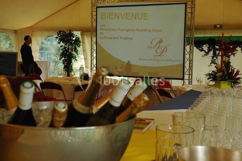Un seau de bouteilles de champagne sur une table, devant une salle de conférence avec écran de présentation.