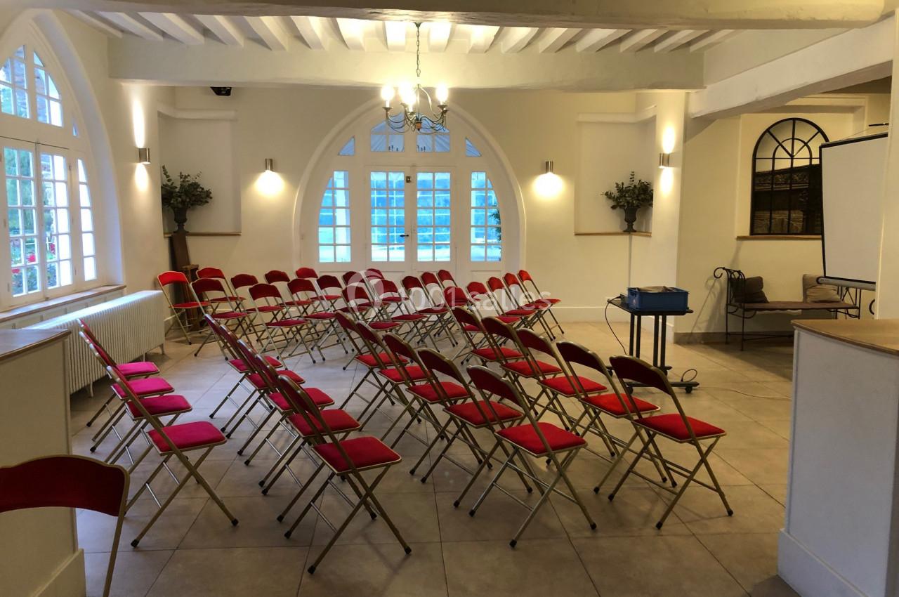 Salle lumineuse avec des rangées de chaises rouges disposées en arc de cercle, écran et projecteur installés.