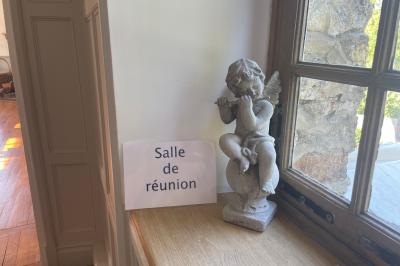 Salle lumineuse avec une grande table rectangulaire couverte d'une nappe bleue, entourée de chaises rouges, et une fenêtre…