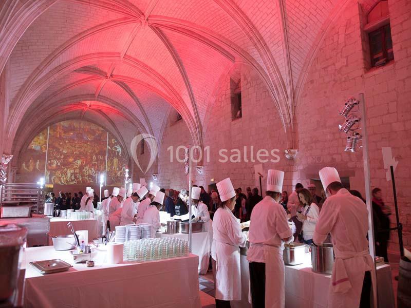 Des chefs en tenue blanche préparent des plats dans une grande salle voûtée éclairée par des lumières rouges.