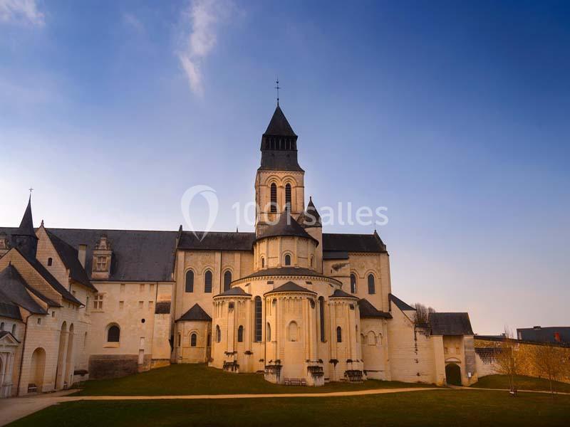 Abbaye en pierre claire avec clocher, entourée d'une pelouse, sous un ciel dégagé en fin de journée.