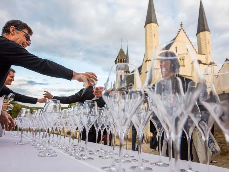 Des personnes échangent des verres à vin sur une table blanche, devant une église aux flèches gothiques.