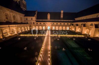 Chambre lumineuse avec lit double, mur beige capitonné, bureau minimaliste, chaise jaune et fenêtre à croisillons.