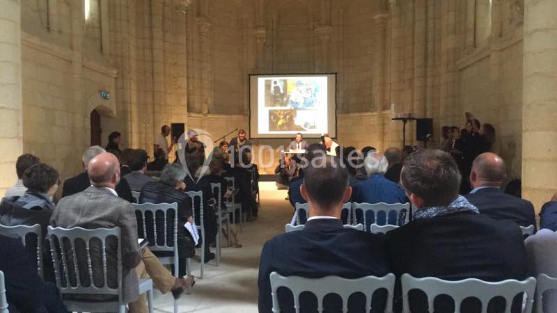 Un groupe de personnes assiste à une présentation avec un écran projetant des images dans une salle en pierre.