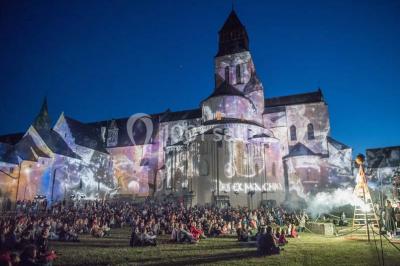 Chambre lumineuse avec lit double, mur beige capitonné, bureau minimaliste, chaise jaune et fenêtre à croisillons.