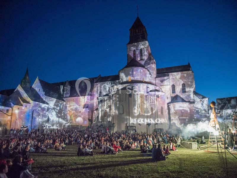 Spectacle nocturne avec projections lumineuses sur une abbaye, devant un public assis sur une pelouse.