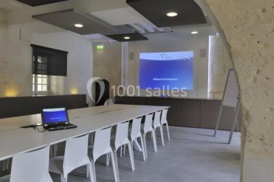 Chambre lumineuse avec lit double, mur beige capitonné, bureau minimaliste, chaise jaune et fenêtre à croisillons.