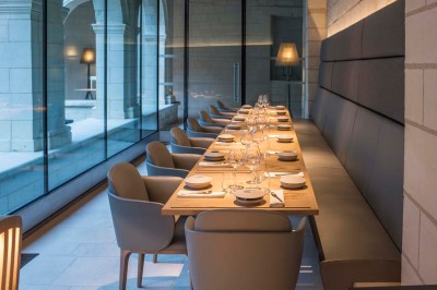 Chambre lumineuse avec lit double, mur beige capitonné, bureau minimaliste, chaise jaune et fenêtre à croisillons.