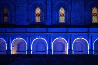 Chambre lumineuse avec lit double, mur beige capitonné, bureau minimaliste, chaise jaune et fenêtre à croisillons.