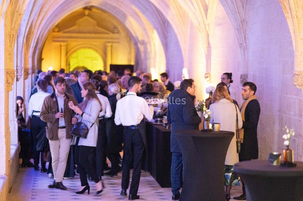 Des personnes discutent et se restaurent dans une galerie voûtée éclairée, lors d'un événement convivial.