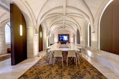 Chambre lumineuse avec lit double, mur beige capitonné, bureau minimaliste, chaise jaune et fenêtre à croisillons.