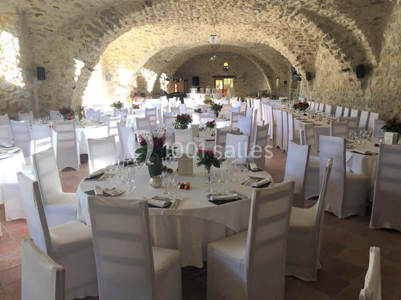 Salle voûtée en pierre aménagée pour un événement, avec tables rondes dressées et chaises blanches.
