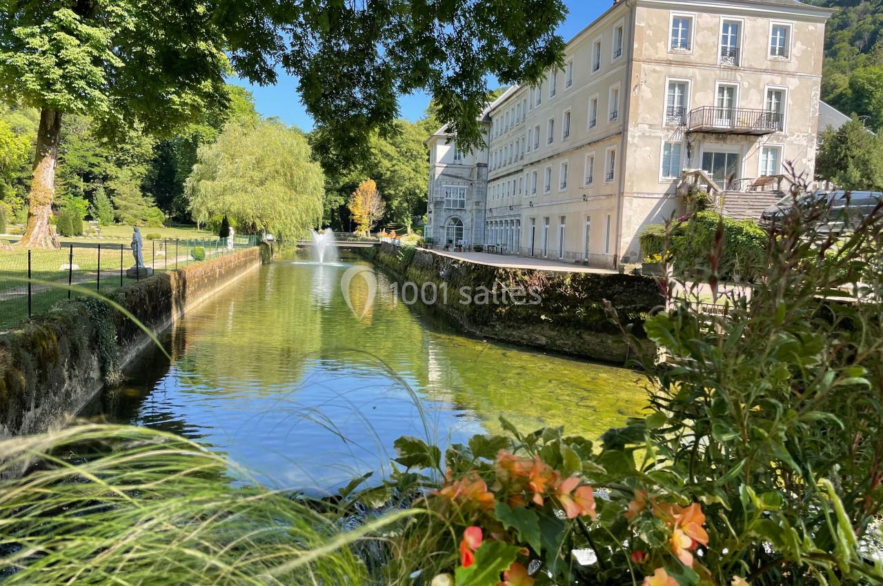 Canal bordé de verdure avec un bâtiment ancien en arrière-plan et des fleurs au premier plan.