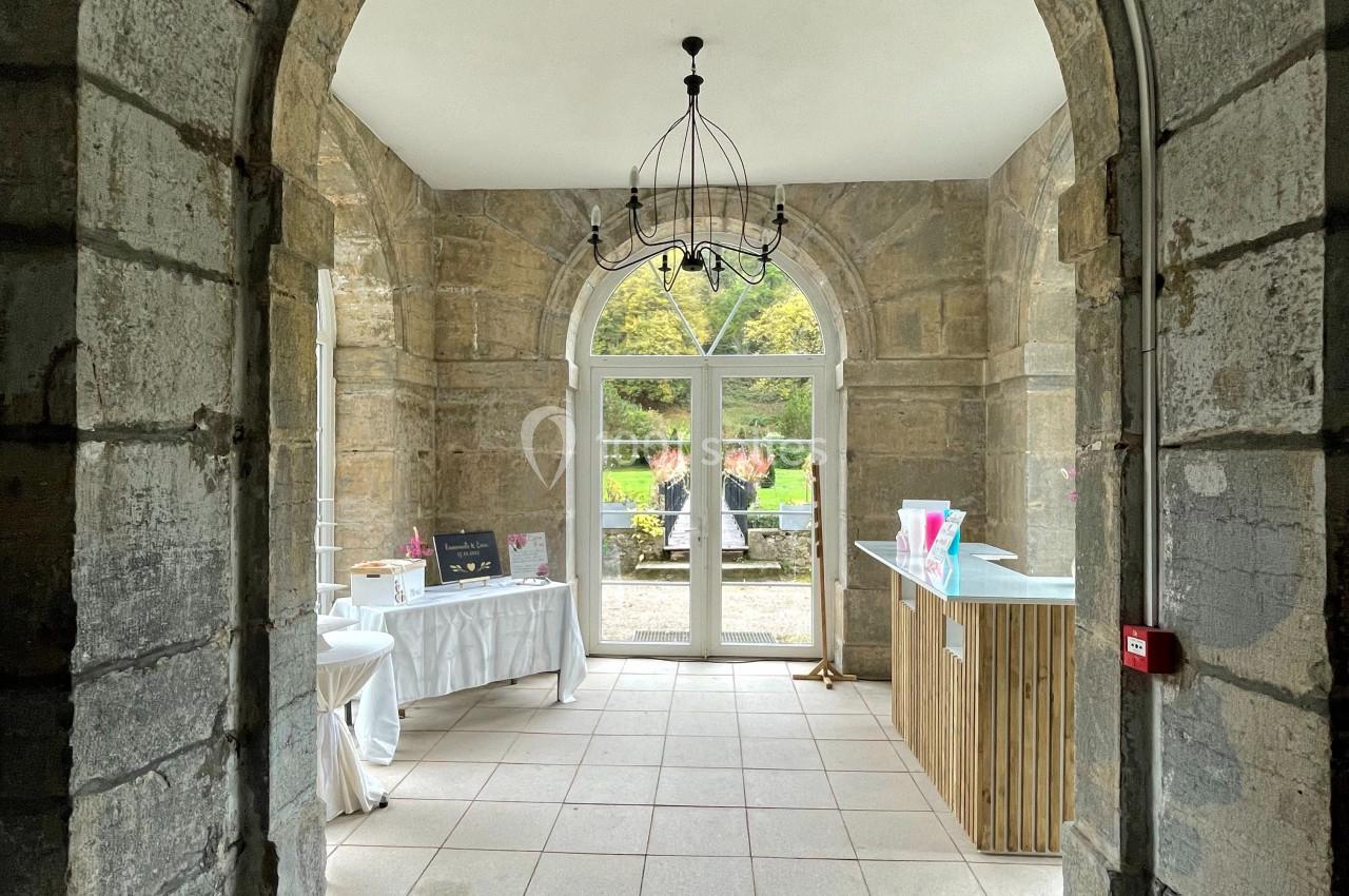 Vue d'un couloir en pierre avec une arche, menant à une pièce lumineuse donnant sur un jardin.
