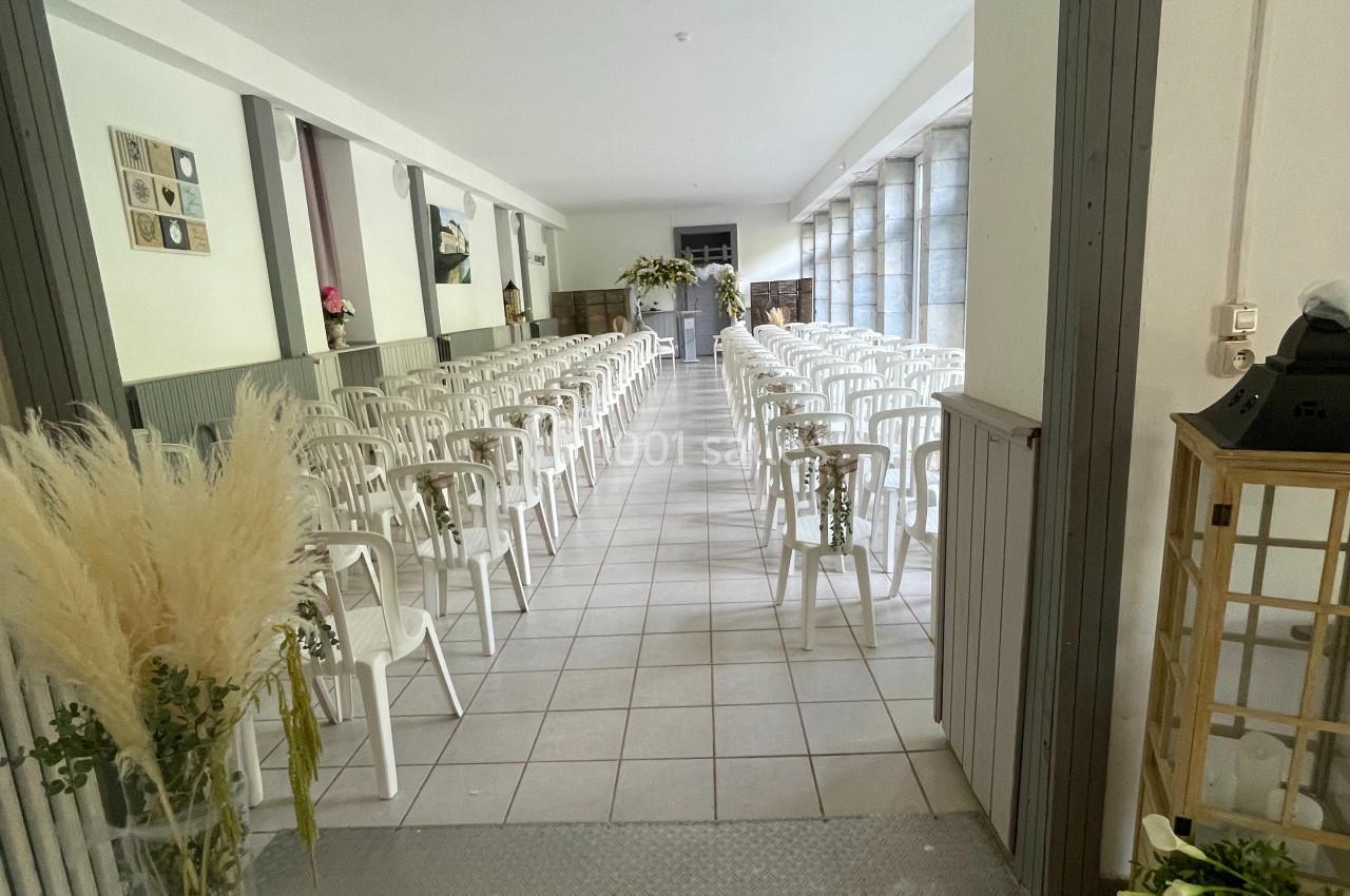 Salle lumineuse aménagée avec des rangées de chaises blanches alignées pour un événement ou une cérémonie.
