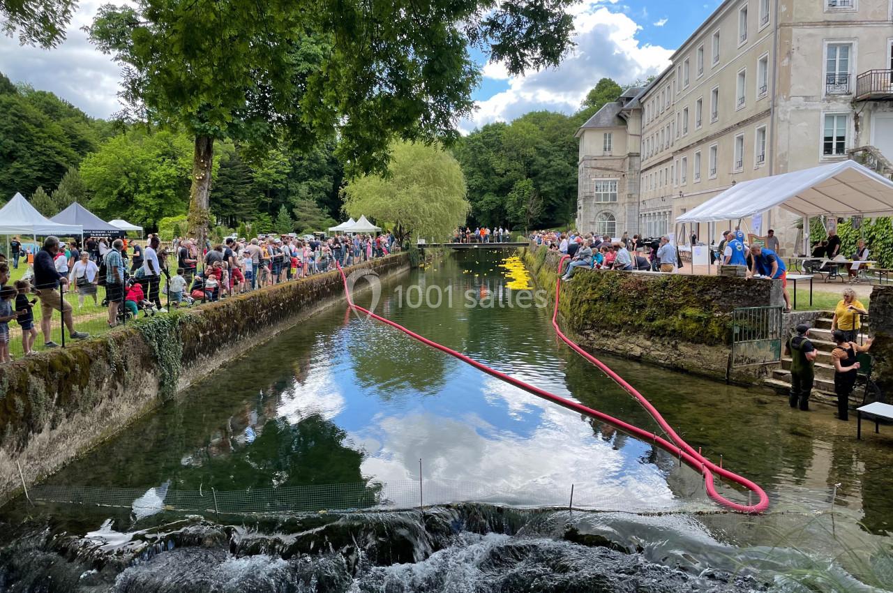 Un canal bordé d'arbres et d'un bâtiment historique, animé par un événement avec des stands et des visiteurs.