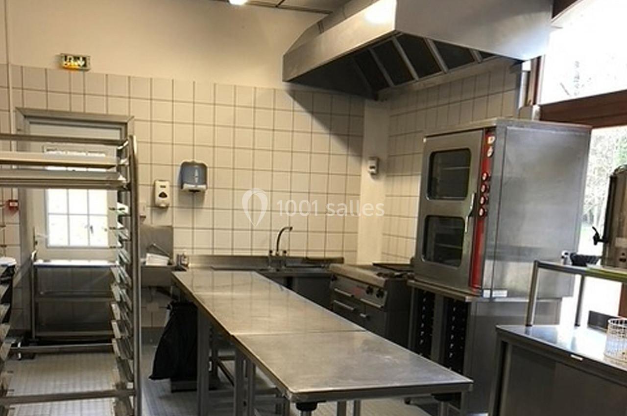 Cuisine professionnelle équipée de plans de travail en inox, fours, étagères métalliques et carrelage mural blanc.