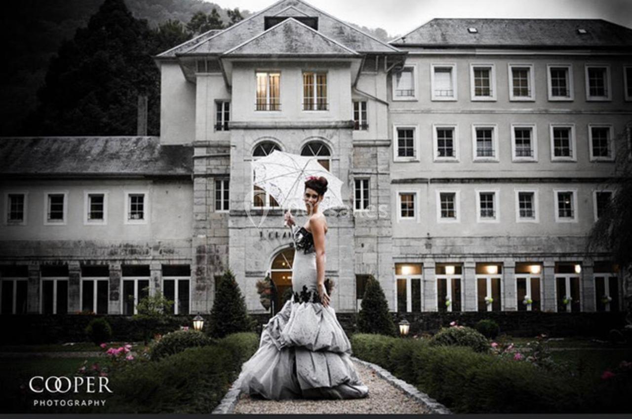 Femme en robe de soirée tenant un parapluie devant un bâtiment historique entouré de jardins.
