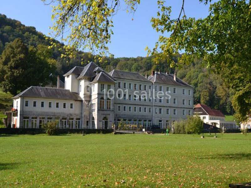 Bâtiment historique entouré de pelouses et d'arbres, situé au pied de collines verdoyantes.