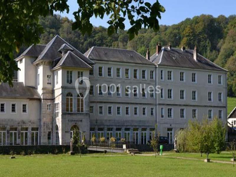 Bâtiment en pierre de plusieurs étages entouré de verdure, avec des arbres et une pelouse au premier plan.