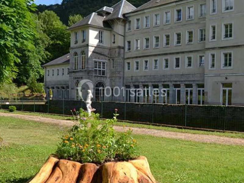 Un bâtiment en pierre entouré de verdure avec un parterre de fleurs au premier plan.
