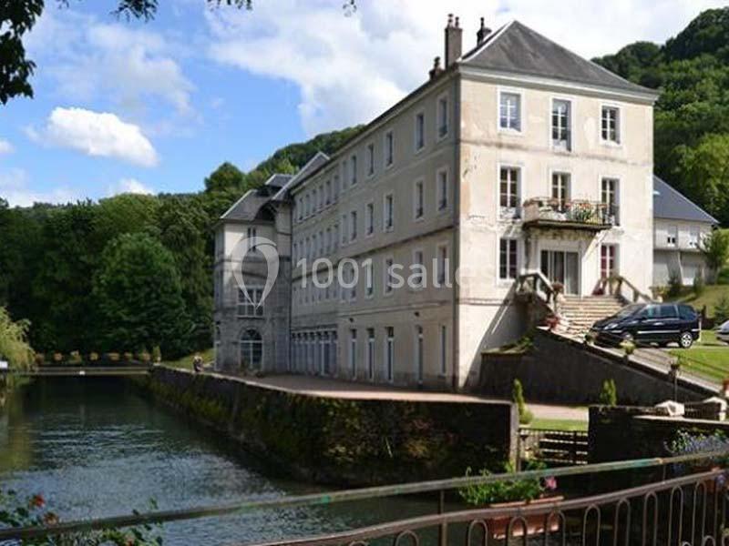 Bâtiment ancien en bord de canal, entouré de verdure, avec une voiture garée près de l'entrée principale.